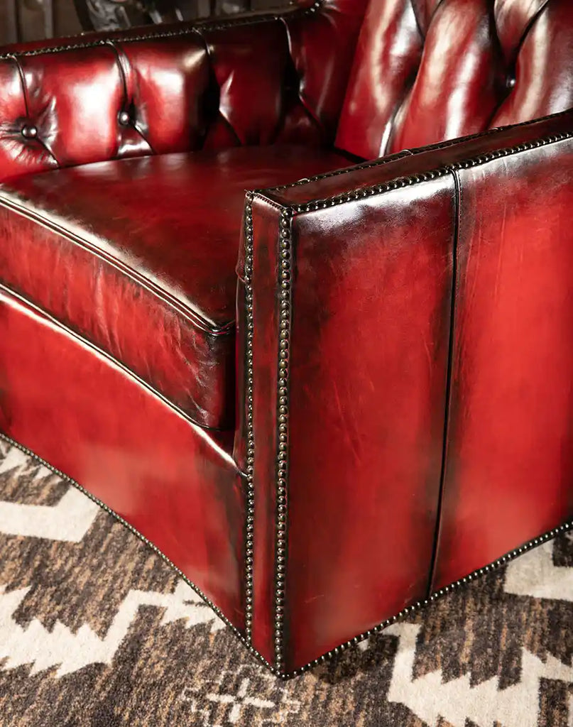 Angled side view of the Cherry Red Swivel Chair, highlighting the luxurious brass nail head trim and smooth swivel base.