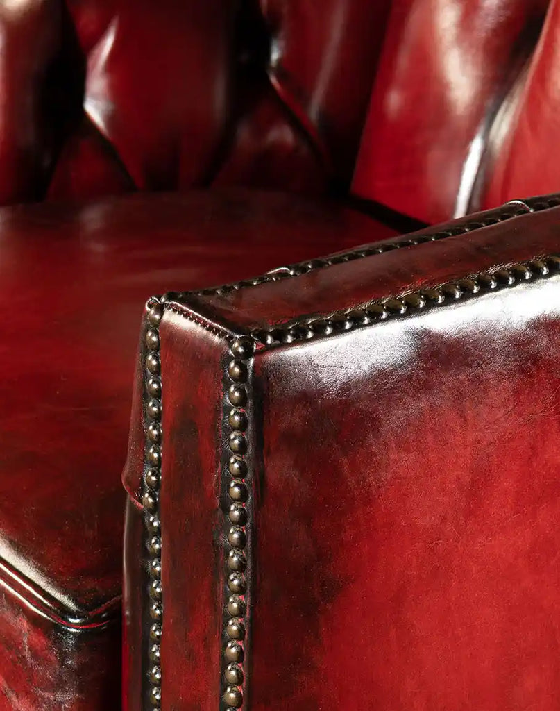 A close-up of the intricate brass nail head trim along the edges of the Cherry Red Swivel Chair, adding a touch of rustic elegance.