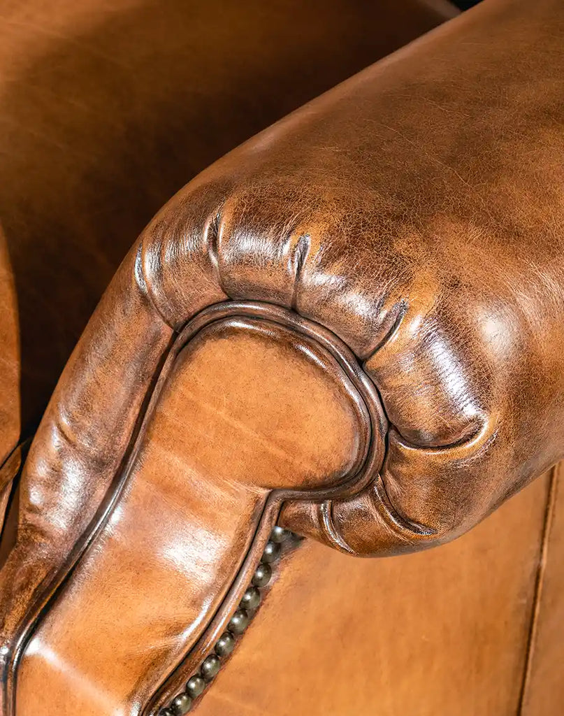 A detailed close-up of the King Arthur Tufted Chair's armrests, featuring hand-burnished full-grain leather and intricate nailhead trim.