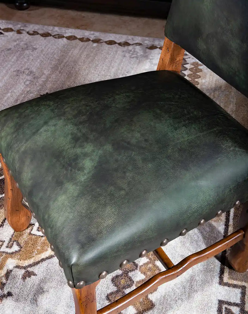 A dining chair with a padded seat and backrest, offering both comfort and style with its forest green leather and axis deer hair back.