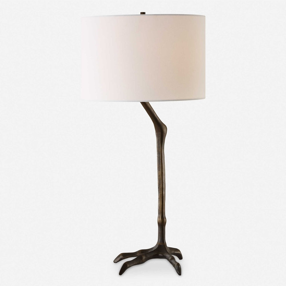 Unique bird-inspired table lamp with a cast iron leg-shaped base in antique bronze and a relaxed white drum shade.