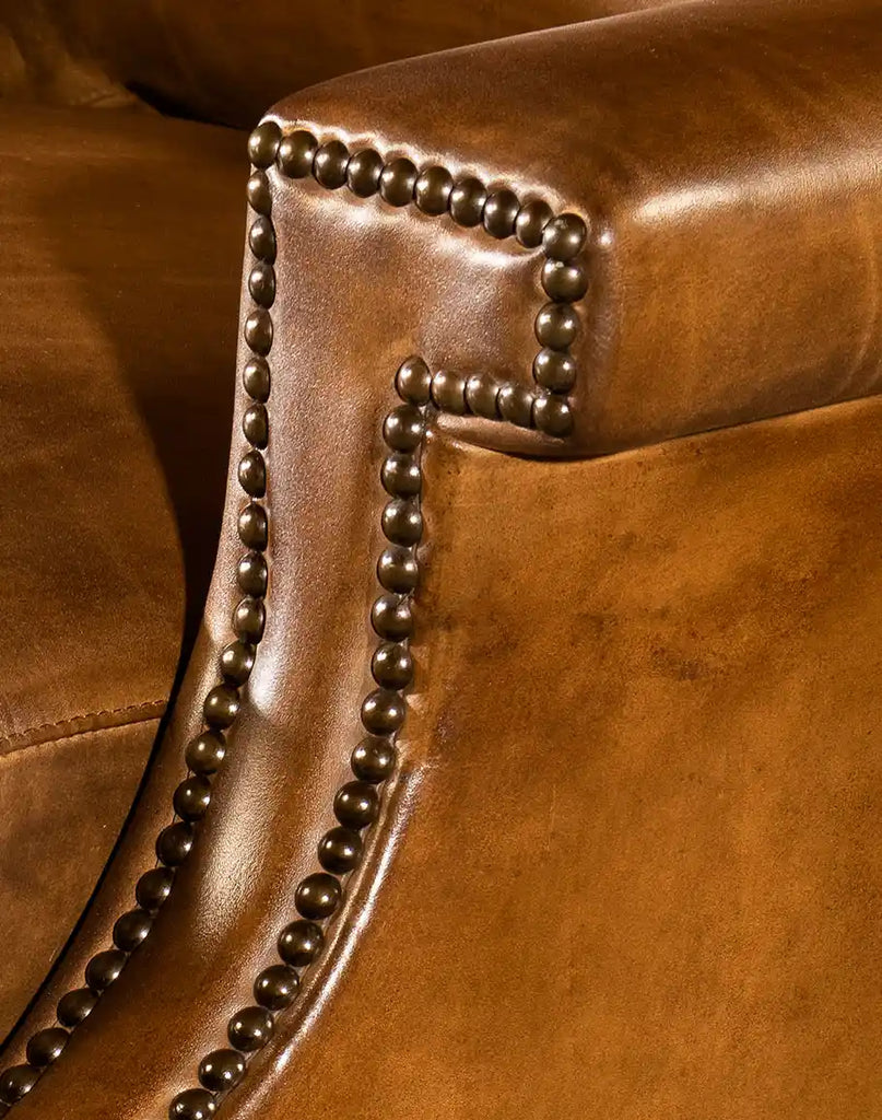 A close-up view of the armrest, featuring intricate nailhead trim accents and luxurious saddle leather.