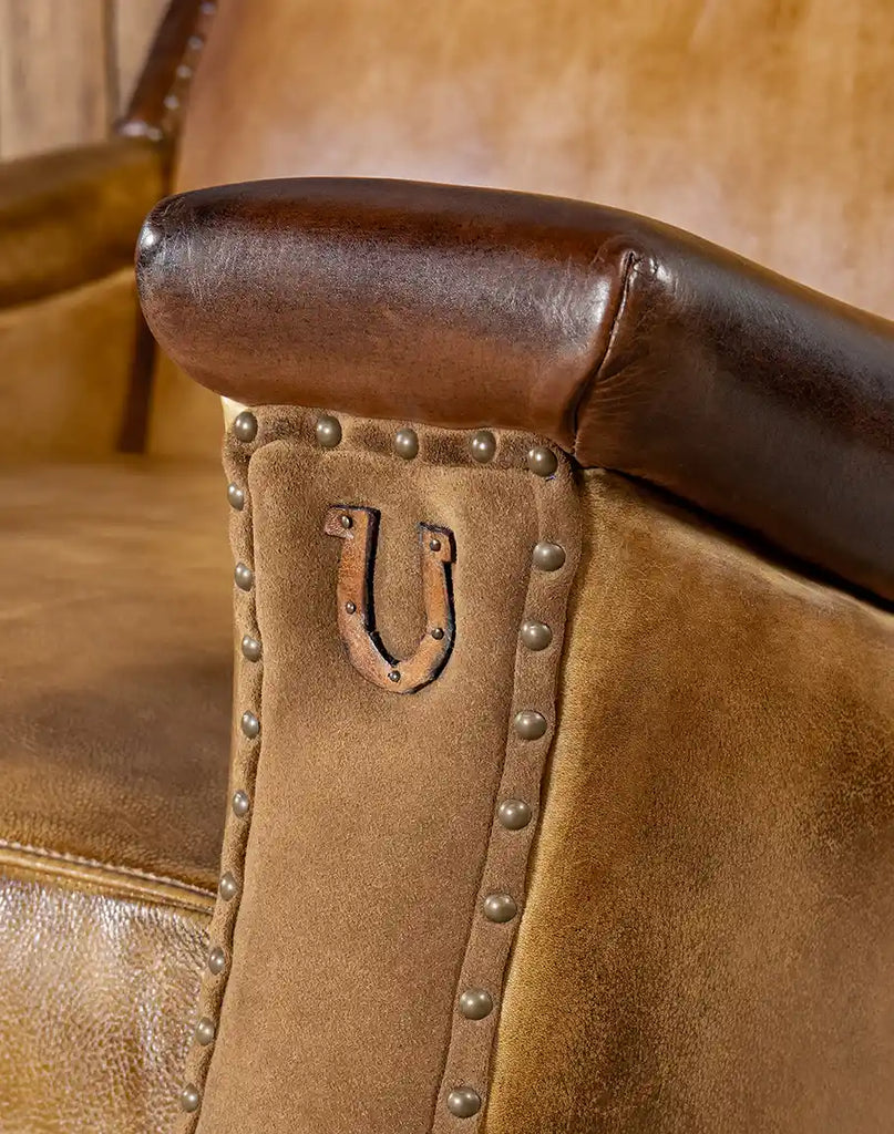 A close-up of the leather horseshoe accent and suede detailing on the arm panels of the Lucy Leather Chair.