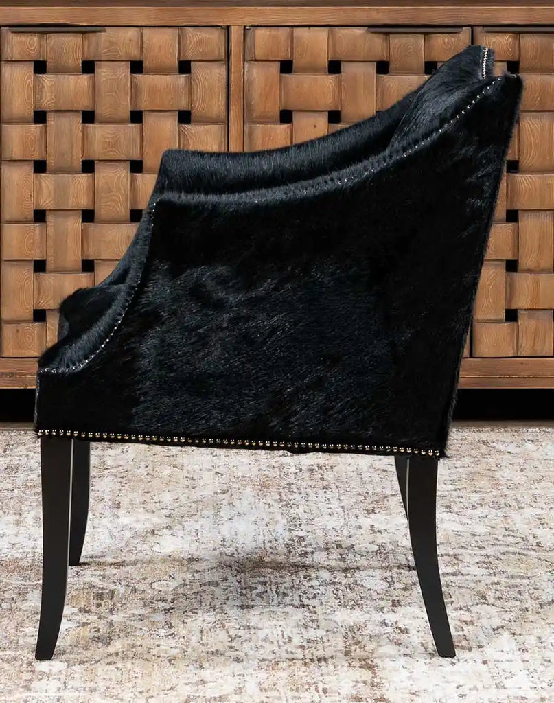 A side-angle view of the McClaren Midnight Cowhide Chair, showcasing its sturdy frame, sloped arms, and cowhide detailing.