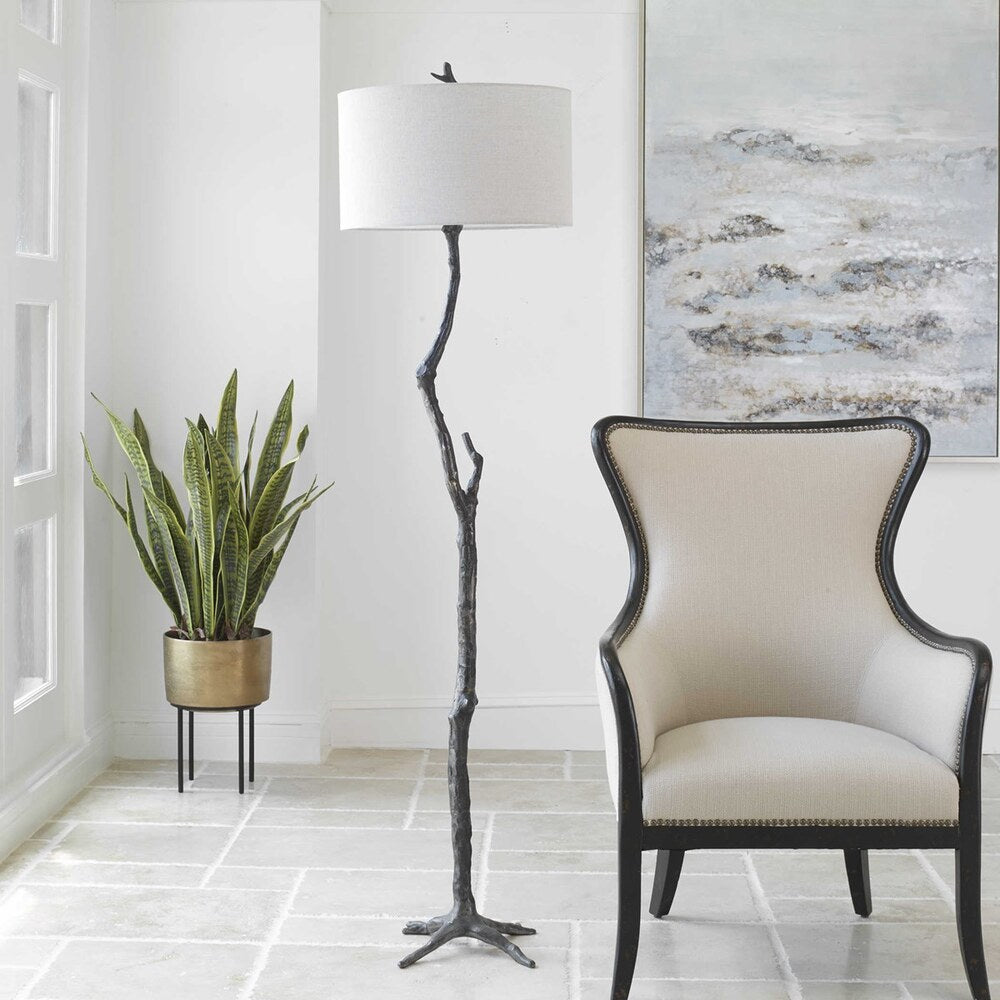 Rustic cast iron floor lamp featuring a sculpted tree branch design with a distressed black finish and silver undertones, topped with a light gray linen shade.