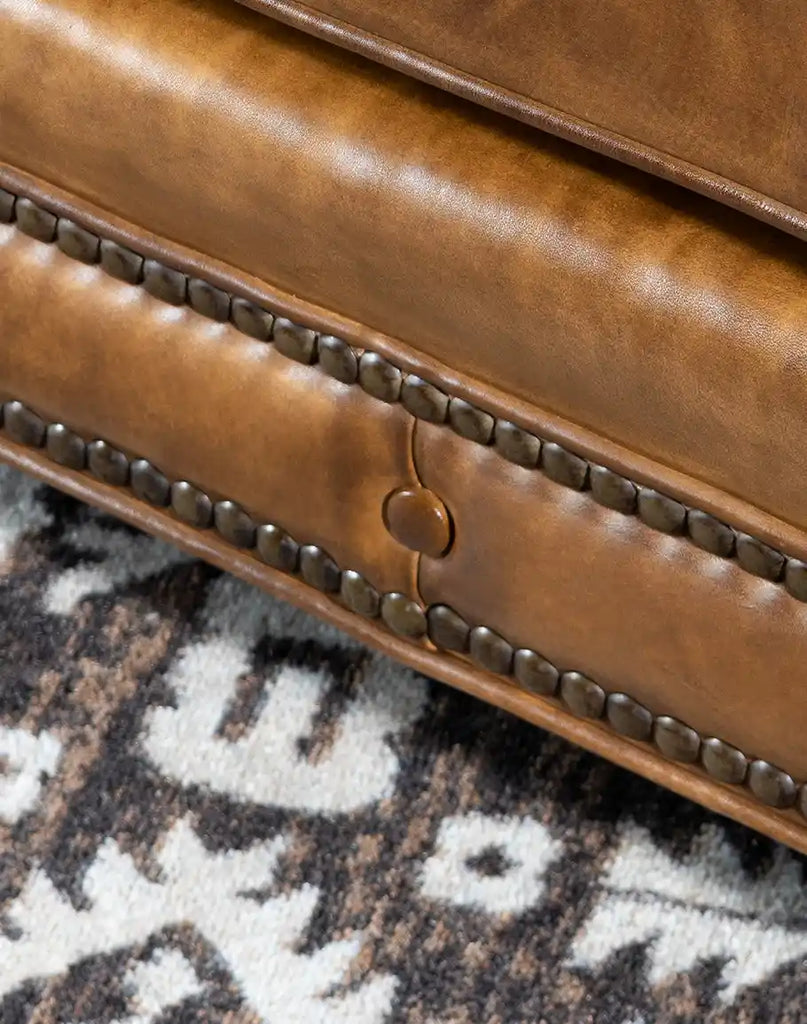 A close-up of the Nova Chesterfield Sofa's hand-burnished leather upholstery with brass nailhead trim, highlighting its intricate detailing and fine craftsmanship.