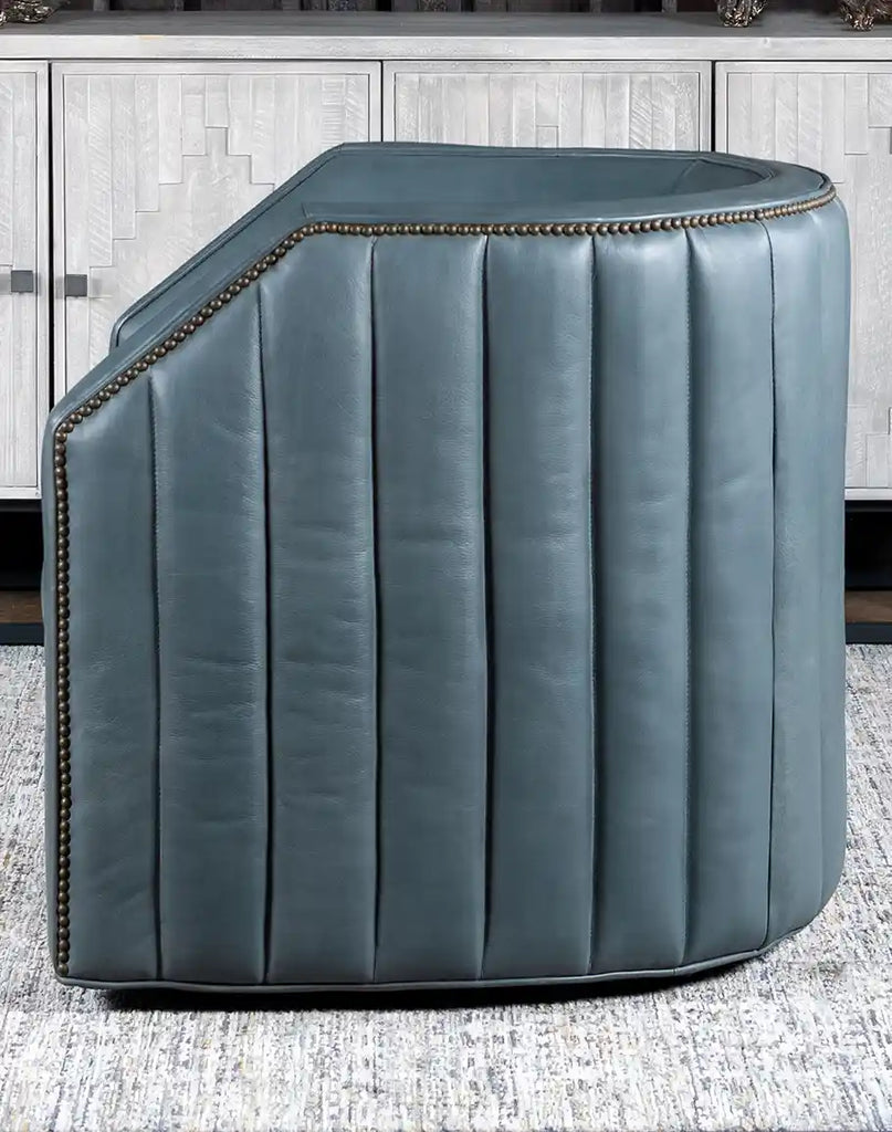 Side view of the Olga Grey Swivel Chair, highlighting its padded channeling and brass nail tack accents.