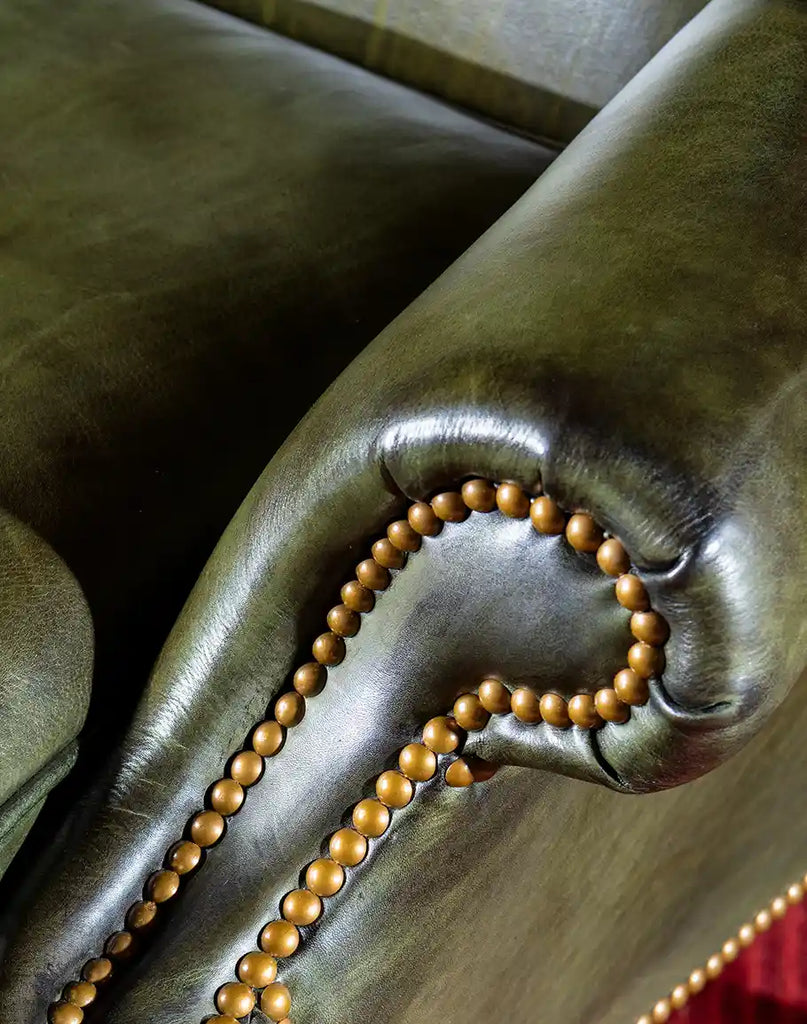 Gold nail tacks accentuating the edges of the armrests on the Olive Green Wingback Chair.