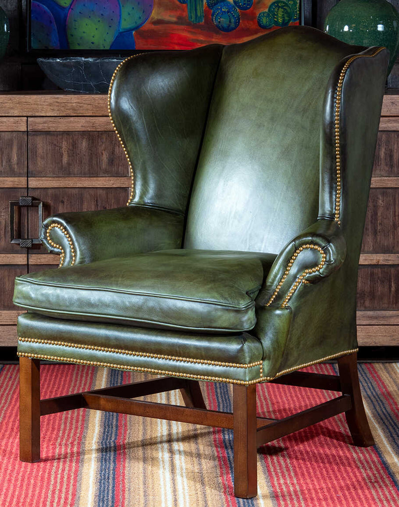 Front view of the Olive Green Wingback Chair with hand-brushed leather upholstery and gold nail tacks.