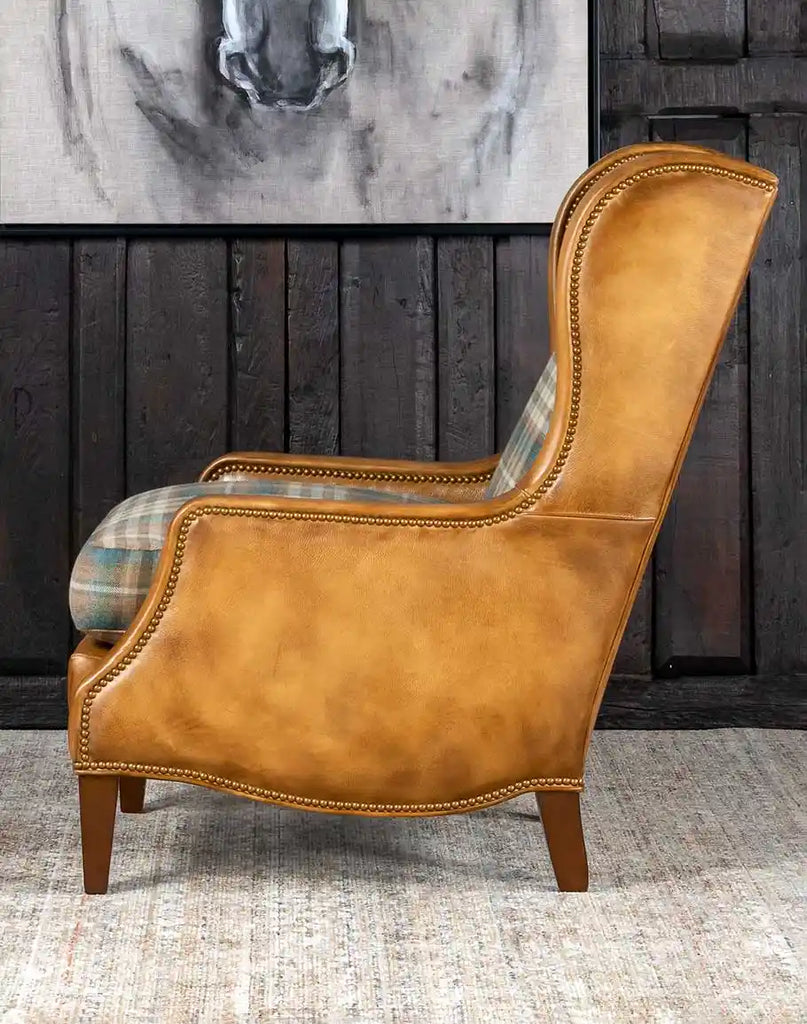 Side profile of the Patterned Spruce Chair featuring the wingback design, brass nail tacks, and smooth leather armrests.