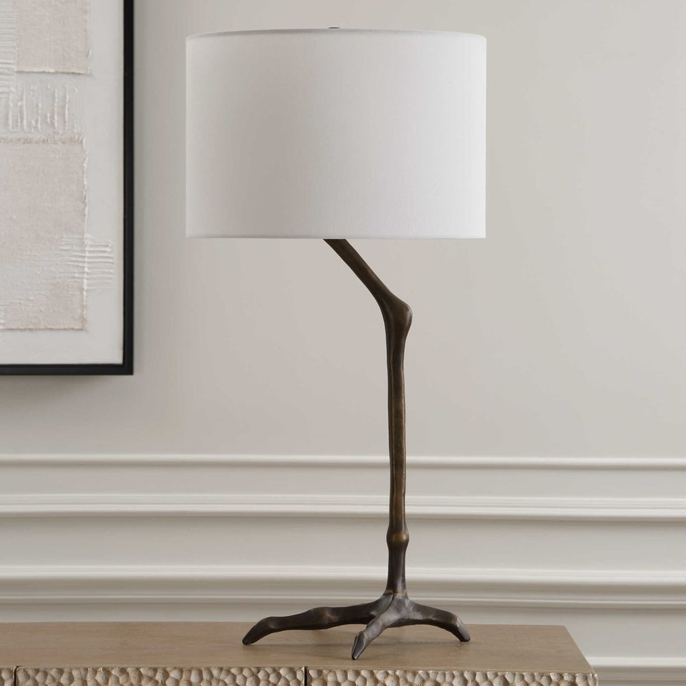 Cast iron table lamp featuring a playful bird-leg design in antique bronze, paired with a soft white linen drum-shaped shade.