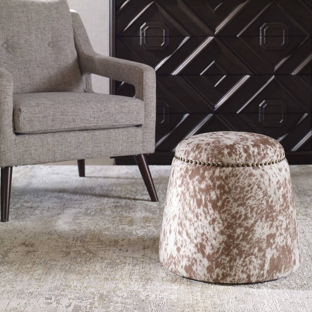 Plush ottoman with chestnut and white faux cowhide upholstery and antique brass nailhead trim.