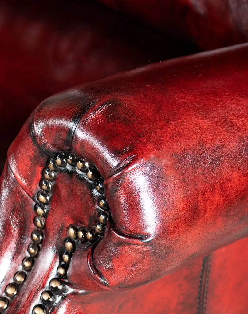 Close-up shot of the Raspberry Leather Recliner's armrest, highlighting the fine craftsmanship and nailhead trim.