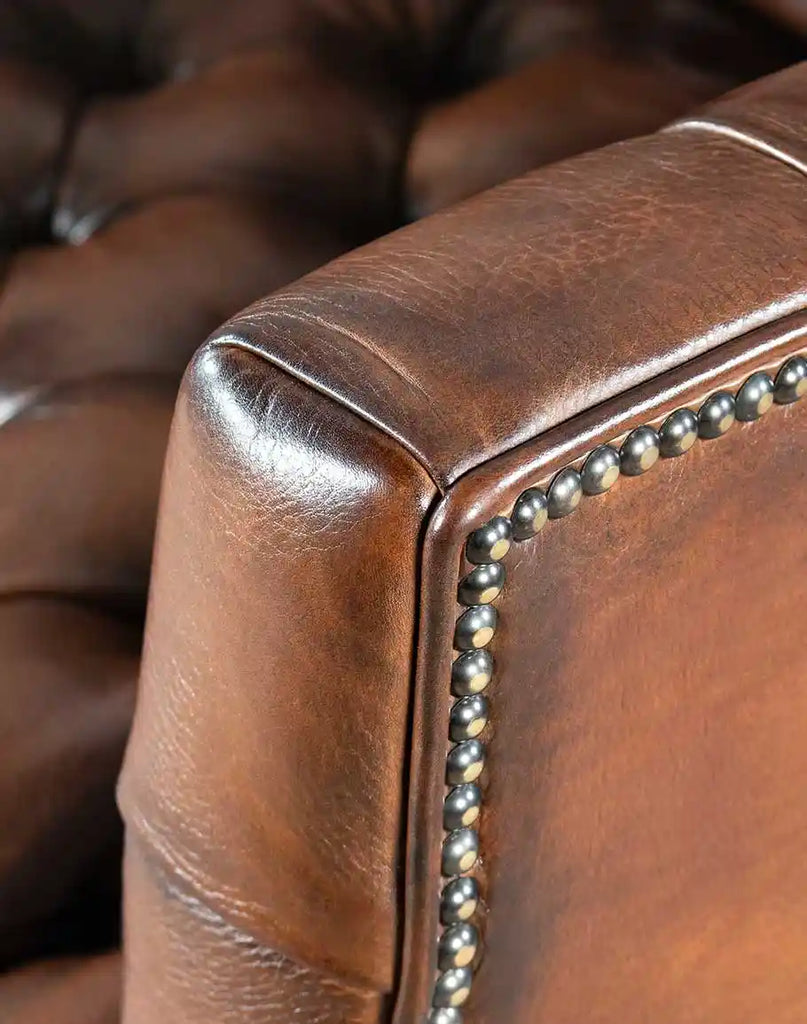 Close-up of the Roan Sable Tufted Leather Chair's armrest, featuring tufted leather and brass nail accents.