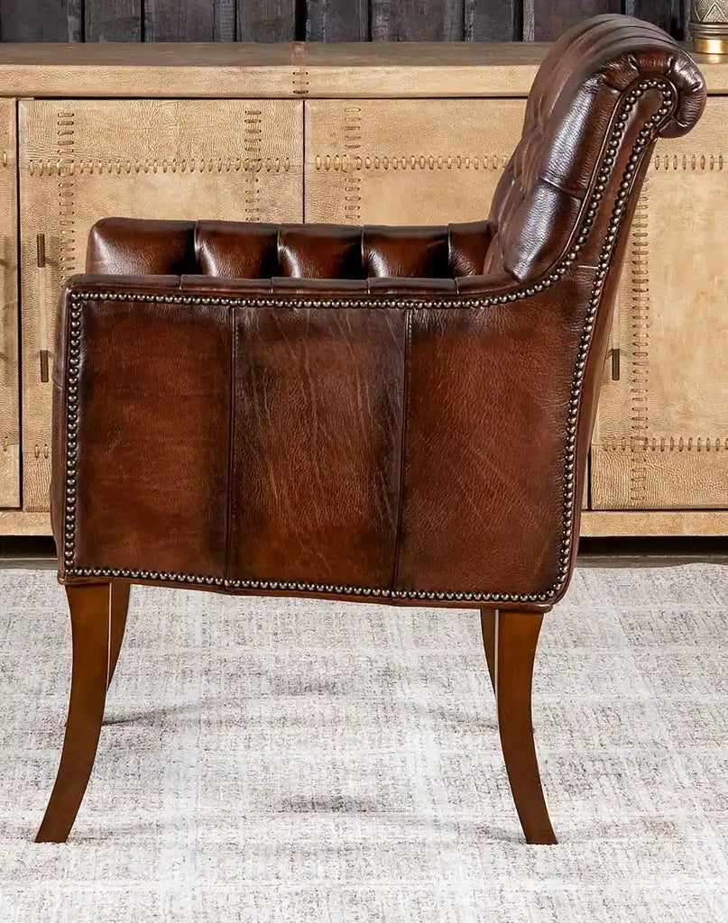 Side profile of the Roan Sable Tufted Leather Chair, emphasizing the gracefully curved legs and brass nail tacks.