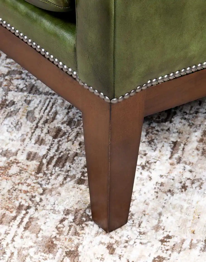 A close-up of the sturdy wooden legs on the Seabrook Moss Leather Chair, finished in a rich stain to complement the leather.