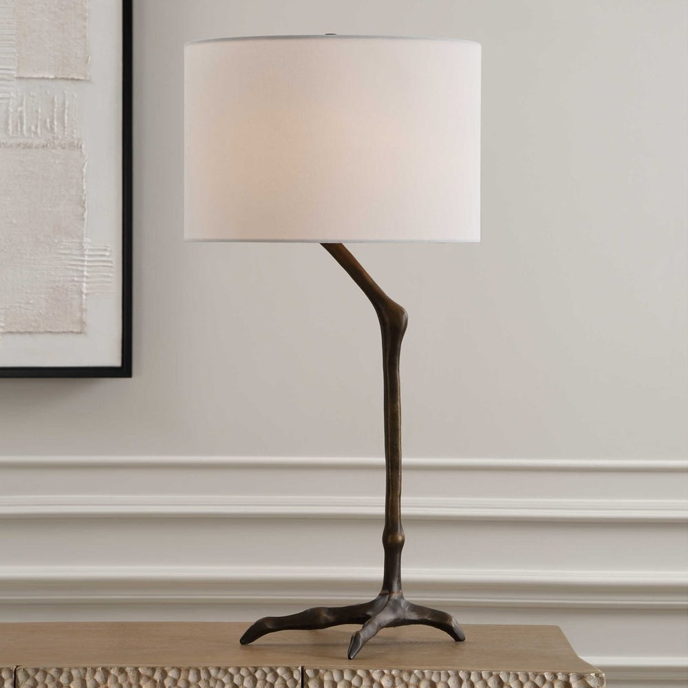 Slender bird-leg table lamp crafted from cast iron, finished in antique bronze, with a round white linen drum shade for modern elegance.