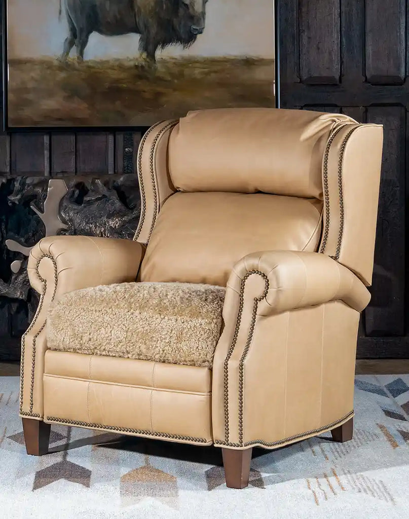 Stanley Sandstone Recliner showcasing its sleek light sand top-grain leather, plush shearling seat cushion, and brass nail tack detailing.