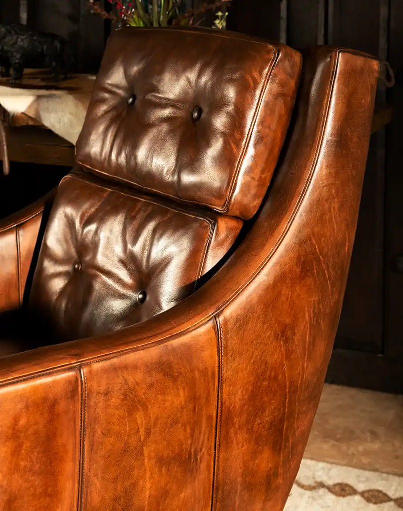 A side profile of the Tan Saddleback Leather Chair, highlighting its curved armrests and fine craftsmanship, perfect for modern and rustic décor.