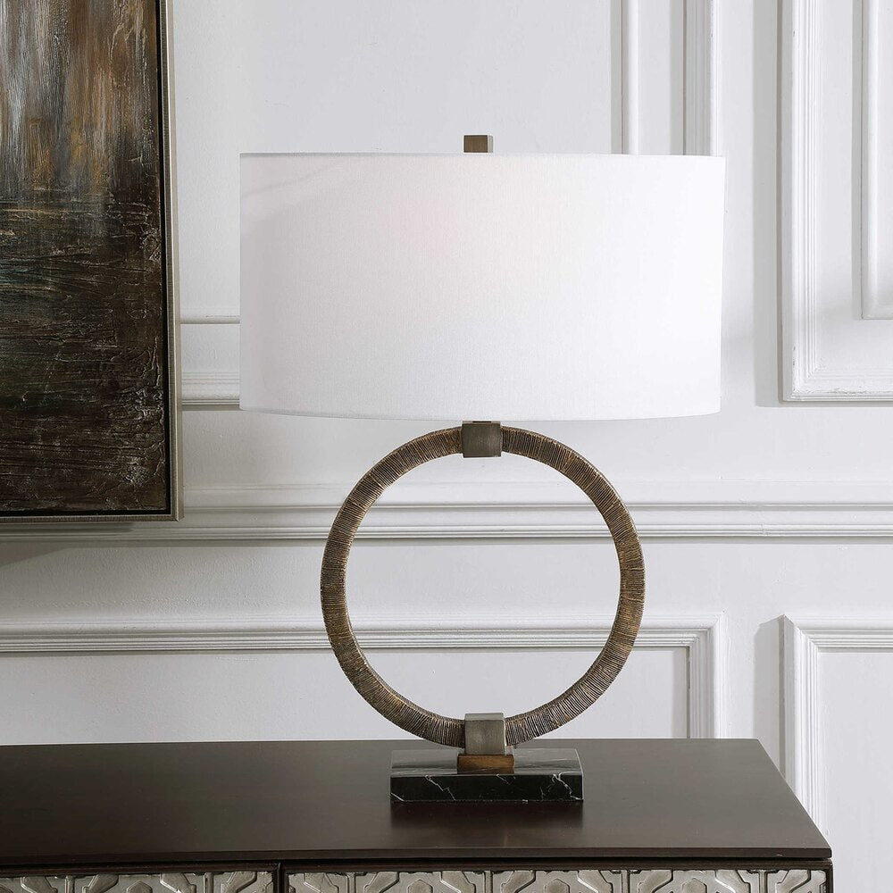 Tribal-inspired table lamp with an antiqued gold hand-carved base, dark bronze accents, and a white linen oval shade on a black marble base.