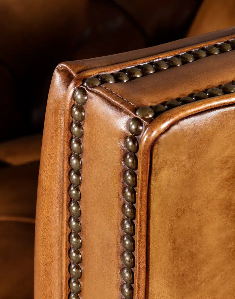 A close-up of the antique-brass nailhead trim on the Kingston Tufted Leather Chair, adding a touch of sophistication.