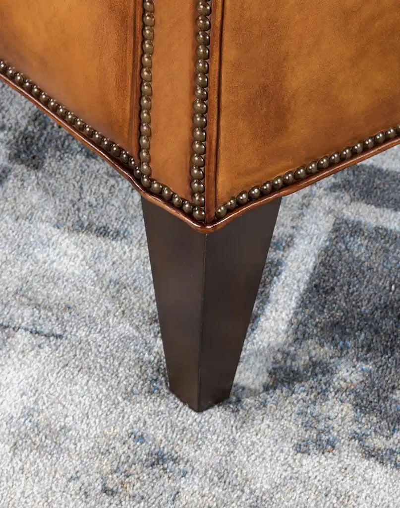 Close-up of the Kingston Tufted Leather Chair’s sturdy wooden leg, featuring a beautifully finished rustic aesthetic.